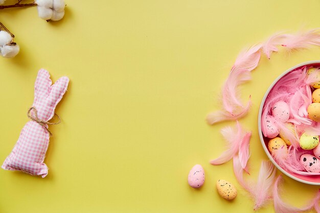 Festive Easter post card concept Pink bowl with colorful eggs pink feathers and handmade cute pink bunny View from above Copy space