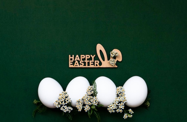 Festive Easter white eggs with white small flowers on a green background Nearby is a wooden inscription Happy Easter