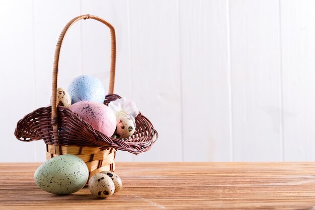 Festive Easter wicker basket with handmade painted chicken and quail eggs on a wooden table.