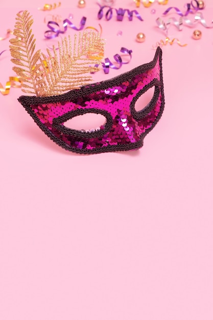 Photo festive face mask for masquerade or carnival celebration on colored background with tinsel vertical format