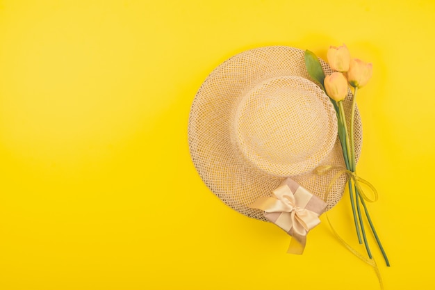 Festive female fashion flat lay with copy space. Gift box, straw hat and yellow tulips 