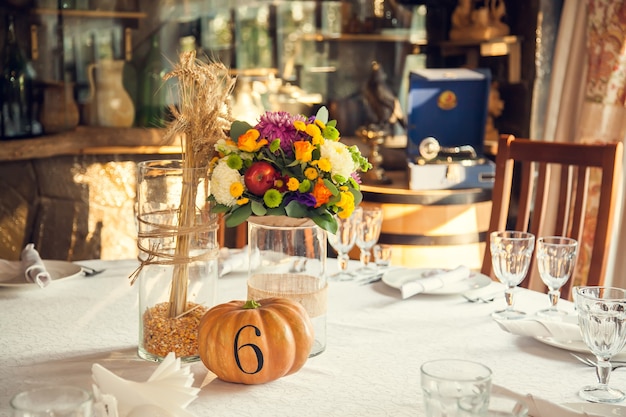 Festive floristry in autumn style with numbering of tables on pumpkins in banquet hall. Floristry and decoration of events floral arrangements.