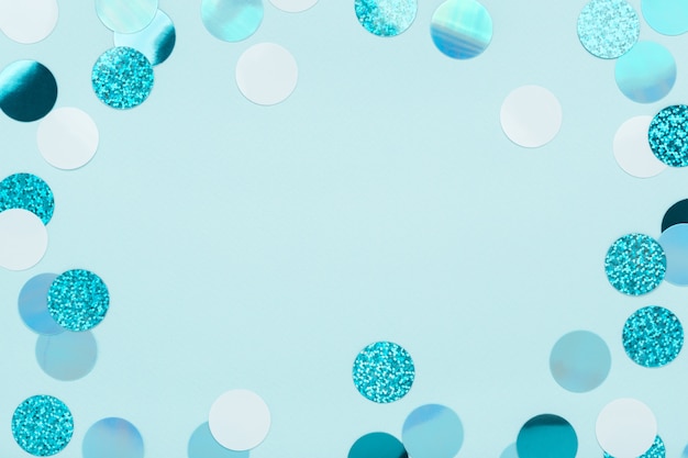 Festive frame of iridescent confetti sparkling on pastel blue background.