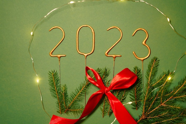 Festive garland around the number 2023 Christmas tree branches and Christmas garland on a green isolated background