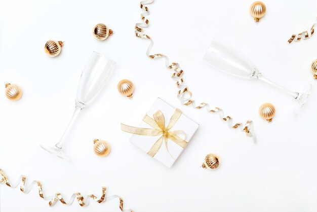 Festive gold flat lay gift box champagne glass and decorative christmas balls white background