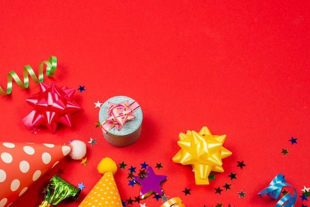 Festive golden and purple stars of confetti and a present birthday caps on a red background Space for text or design