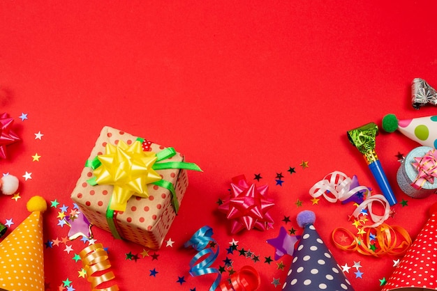 Festive golden and purple stars of confetti and a present birthday caps on a red background Space for text or design