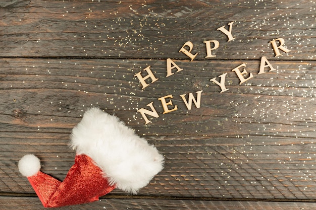 Festive greeting card for new year with red santa hat and wooden text scettered out of it on a table copy psace for text