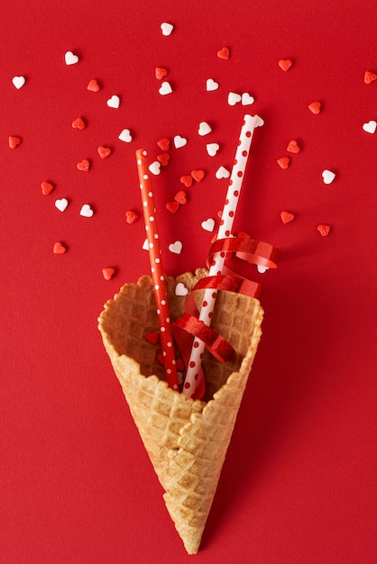 Festive ice cream cone with decorations and confetti on red backgrond, top view flat lay. Creative minimalism concept