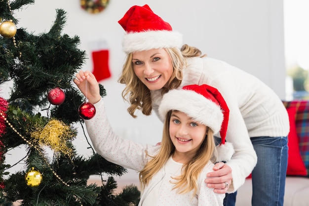 Madre festiva e figlia che decorano l'albero di natale