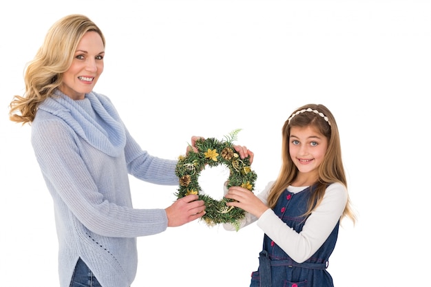 Festive mother and daughter holding christmas wreath