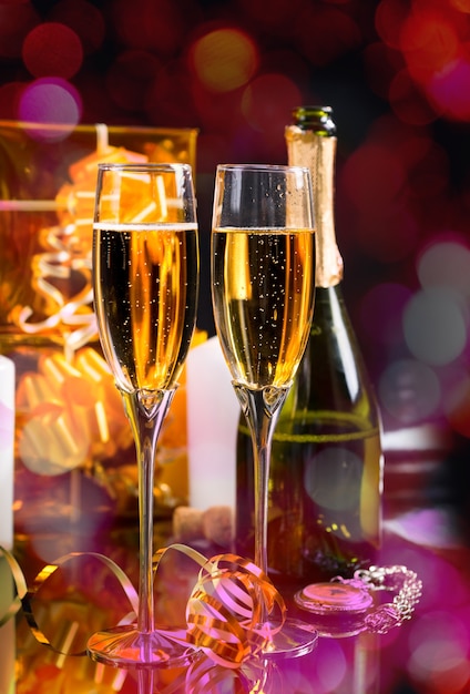 Festive New Year Still Life - Two Glasses of Sparkling Champagne with Bottle, Pocket Watch and Gold Wrapped Gifts on Shiny Background