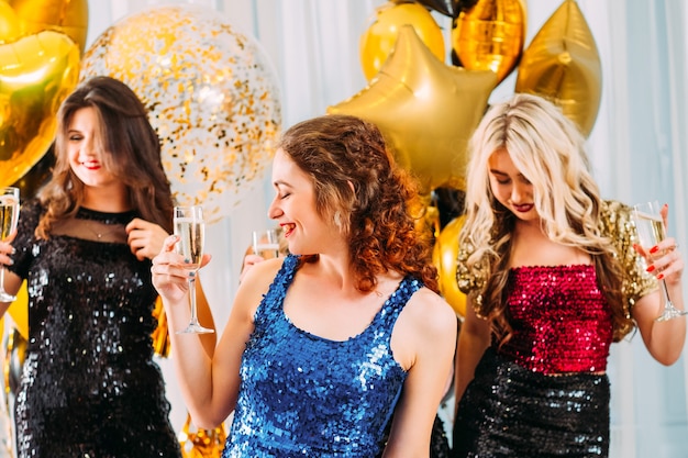 Festive occasion. Cheerful girls celebrating special day with champagne. Ladies wearing shiny dresses, having fun.
