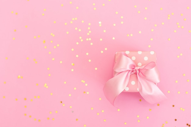 Festive pink background. Gift with satin bow and shining stars on light pink pastel background.