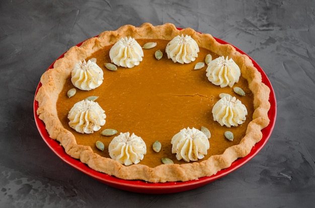 Festive pumpkin pie with spices, whipped cream and seeds