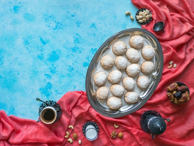 Festive Ramadan sweets are served with tea on the blue table. Egyptian cookies "Kahk El Eid" - cookies of El Fitr Islamic Feast. Top view