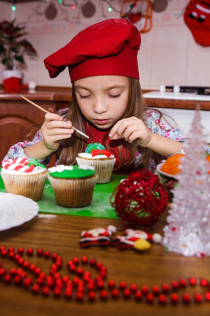 お祝いの赤いエプロンクリスマスパーティーディナーデザートペパーミントカップケーキチーズクリームシュガー振りかける装飾