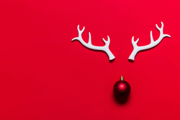 Festive reindeer face made from white antlers and a christmas tree bauble on a red background