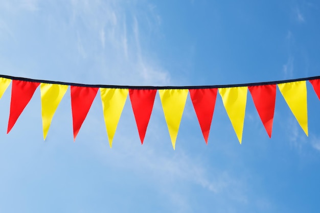 Festive ribbon of red and yellow triangle flags on the white clouds and blue sky background