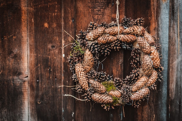 Festive rustic Christmas wreath of pine cones on a dark brown wooden wall.