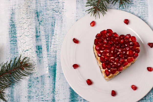 Festive salad in the shape of a heart, decorated with pomegranate seeds on a blue background for Valentine's Day, Horizontal orientation, Copy space