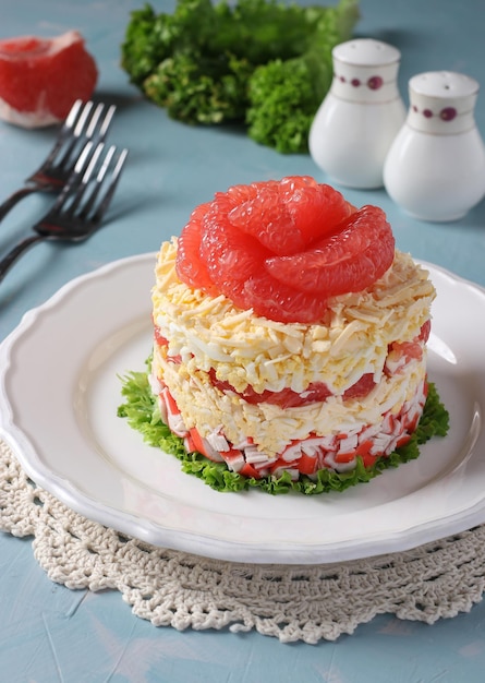 Festive salad with grapefruit cheese and crab sticks on a white plate on light blue background Vertical format