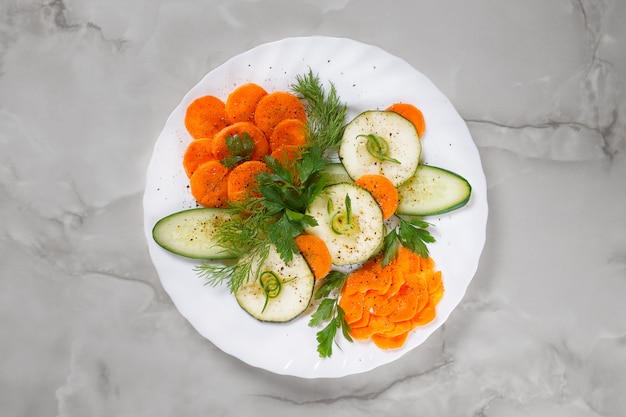 Festive slicing of fresh vegetables with parsley and dill on a white plate on a gray marble background.