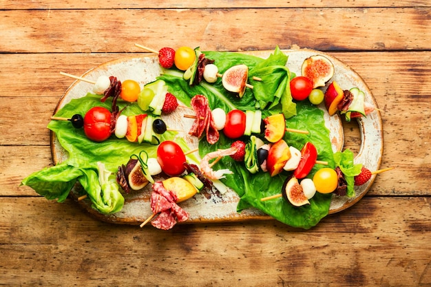 Festive snack of shrimps jamon fruits and vegetables on wooden skewers