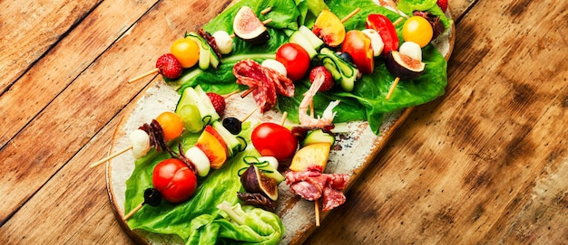 Festive snack of shrimps jamon fruits and vegetables on wooden skewers