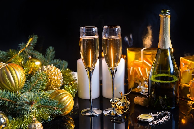 Festive Still Life - Two Glasses of Sparkling Champagne with Bottle, Candles, Gifts, Pocket Watch and Christmas Decorations on Black Background