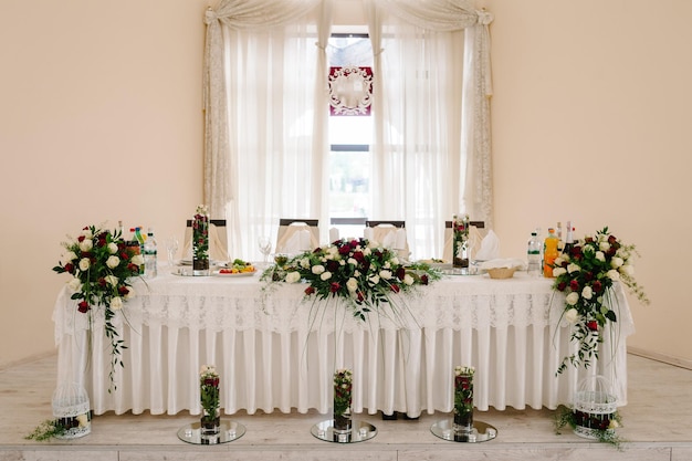 Supporto ad arco da tavolo festivo decorato con una composizione di fiori bianchi rossi e candele verdi nella sala banchetti tavolo sposi novelli nell'area banchetti sulla festa di matrimonio