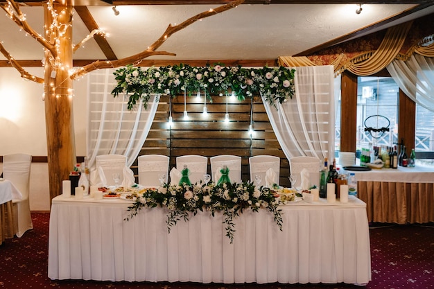 Festive table arch stands decorated with composition of white flowers and greenery candles in the banquet hall Table newlyweds in the banquet area on wedding party