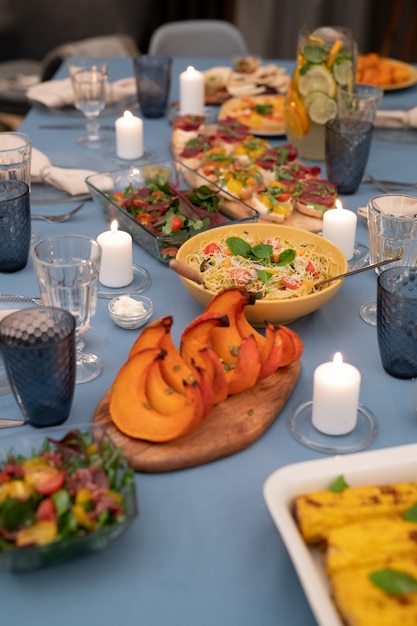 Festive table served with wineglasses, burning candles, vegetable salad, homemade sandwiches, pasta, baked pumpkin slices and grilled corn