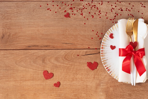 写真 バレンタインデーのフォーク、ナイフ、赤の弓、木製のテーブルの上の心のお祝いテーブルの設定。テキストのためのスペース。上面図