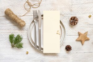 Festive table setting of plates, cutlery and fir tree branches top view. mockup of christmas or new year menu on white wooden table, copy space. winter wedding, restaurant holiday catering