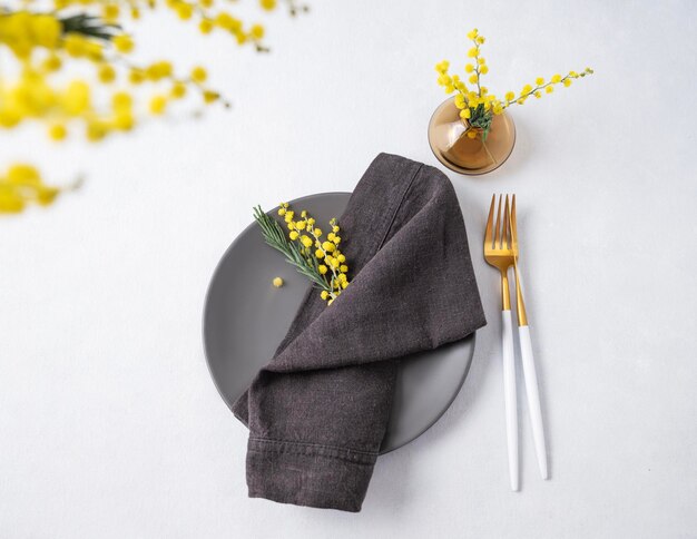 Festive table setting for the spring celebration of women's day birthday or mother's day with yellow mimosa flowers on a light background with dark napkin