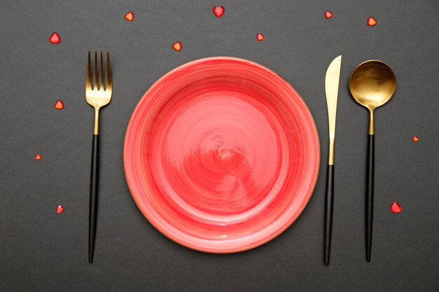 Festive table setting for Valentines Day with fork, knife and hearts on a black table. Top view.