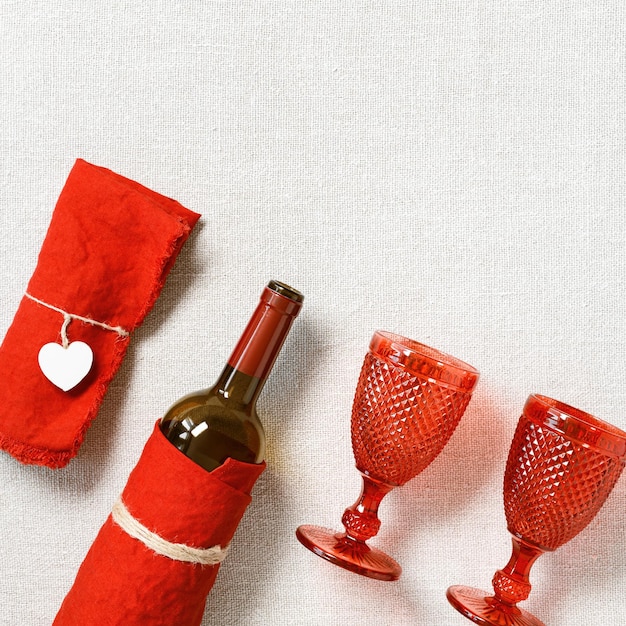 Festive table setting for Valentines Day with red glass colored wine glasses bottle of red wine