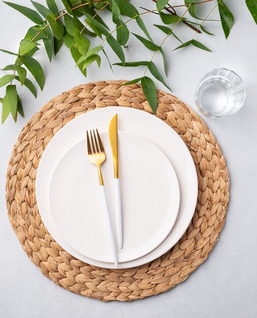 Festive table setting with white plates glass and cutlery on a light background with napkin and eucalyptus branches Restaurant menu concept Top view