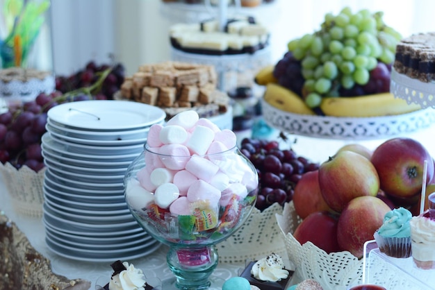 Photo festive table with marshmallow and jelly in a glass bowl and on the background are fruits