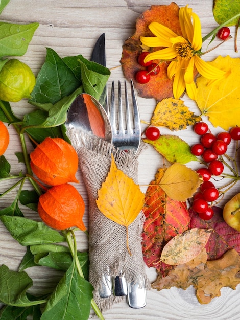 Праздничная осенняя установка столовых приборов на День благодарения и композиция из красочных осенних листьев, красных ягод