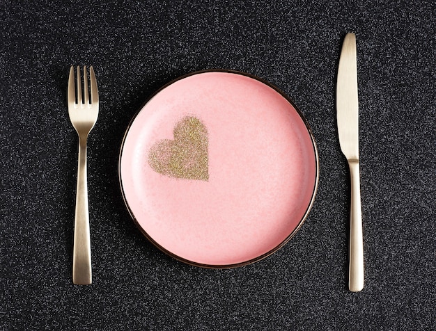 Festive Valentine's Day table setting, pink plate with golden hearts on black shiny background