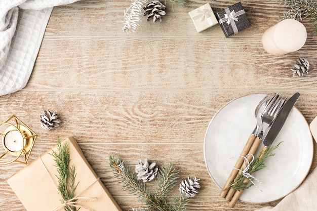 Festive wooden table setting with winter decorations, cutlery, candles and gifts. Top view, flat lay. The concept of a Christmas family dinner.