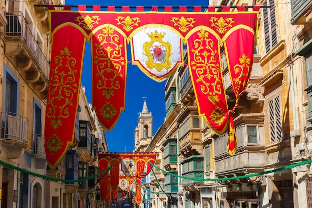 Festively decorated street with banners for St Augustine Feast in the old town of Valletta, Malta. Flaming, arrow pierced heart - symbol of St Augustine
