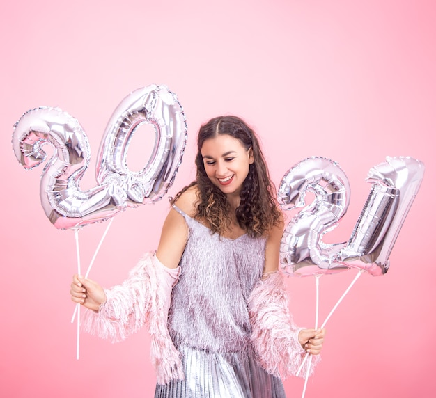 Празднично одетая молодая женщина мило улыбается на розовой стене с серебряными шарами для новогодней концепции
