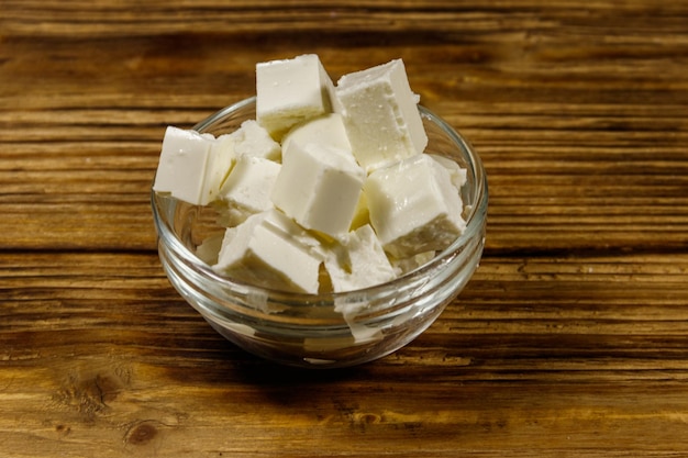 Feta cheese cubes in glass bowl on a wooden table