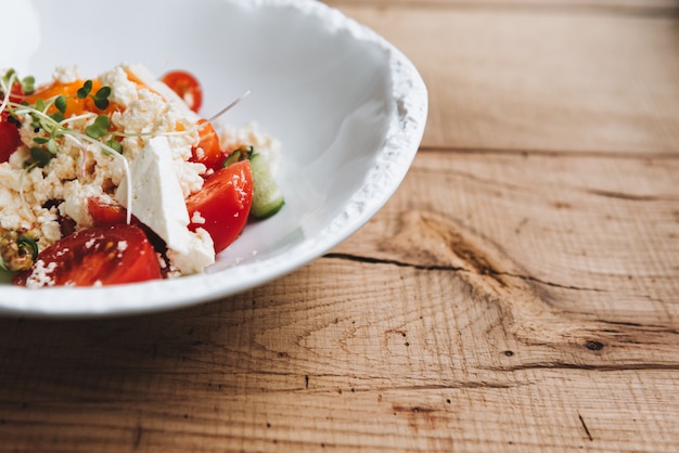 Feta cheese and tomato salad with green peas sprouts on white plate on a wooden surface