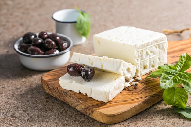 Photo feta cheese with olives and basil on a bamboo chopping board the most famous greek cheese