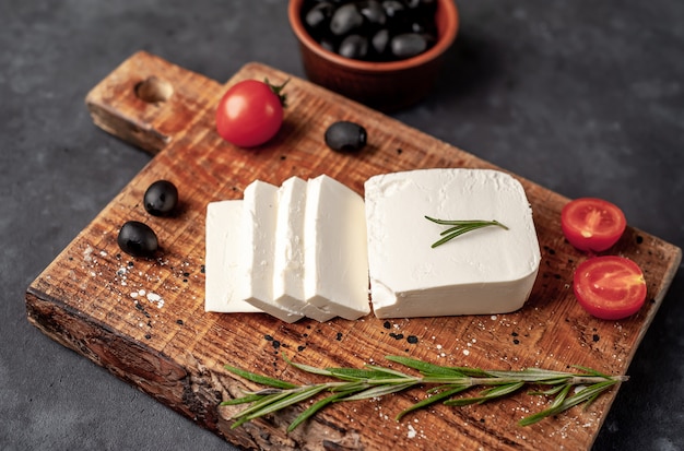 Photo feta cheese, with rosemary, tomatoes, olives on a stone background.