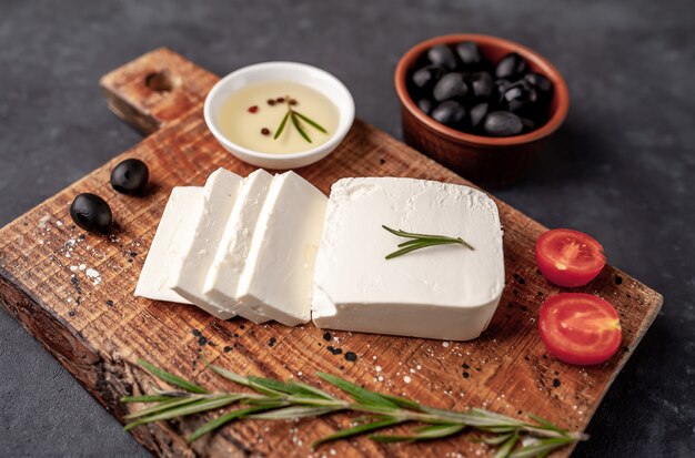 feta cheese, with rosemary, tomatoes, olives on a stone background.